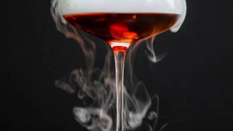 The Vampire Cynar Negroni, dark red cocktail in coupe with dry ice fog, rosemary sprig