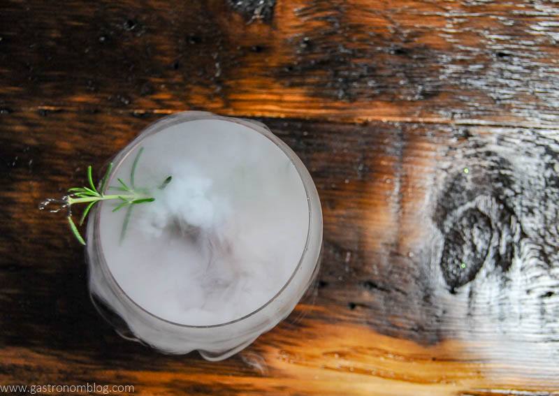 top view of Dry ice boils out rolling fog from a red Cynar Negroni in a cocktail coupe