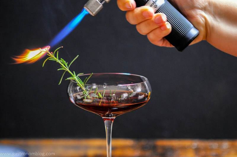 Cocktail in a coupe. Flame on a rosemary sprig. 