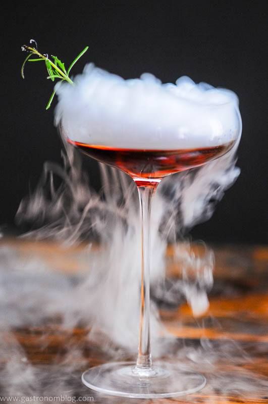 Cocktail in a coupe, rosemary sprig. Dry ice fog over the whole glass. 
