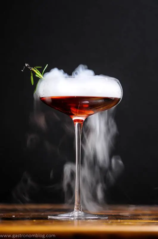 Dry ice boils out rolling fog from a red Cynar Negroni in a cocktail coupe