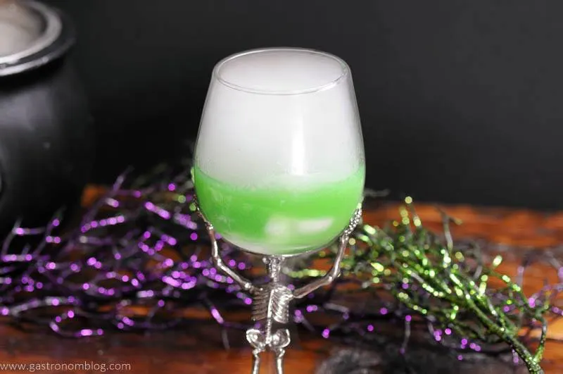 Green Fantastic Beasts cocktail in skeleton glass with dry ice, cauldron in background