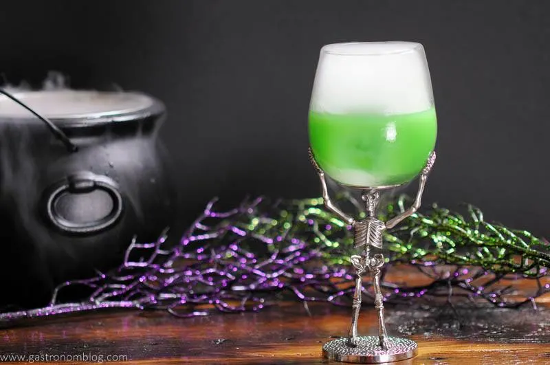 Green Fantastic Beasts cocktail in skeleton glass with dry ice, cauldron in background.