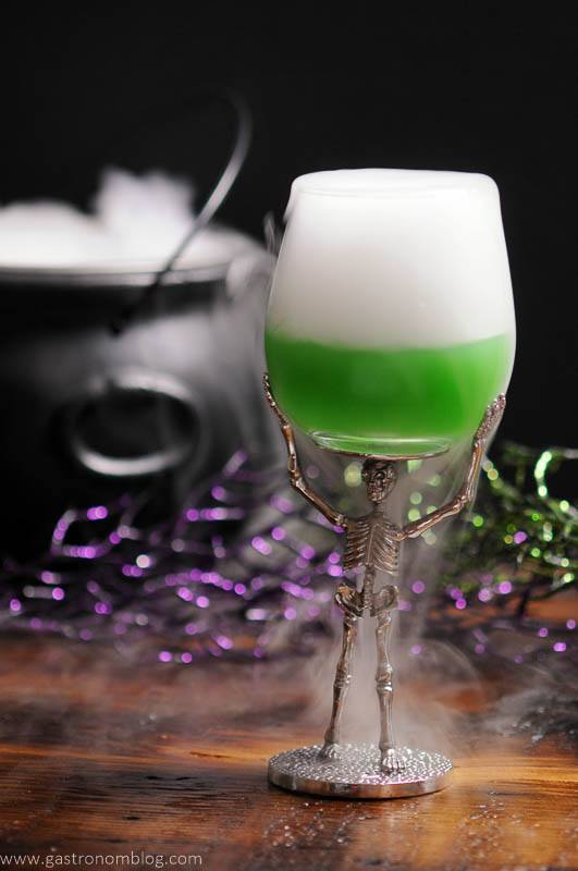 The Grindlewald Goblet - A creen cocktail in a skeleton wine glass with dry ice smoke coming from it.