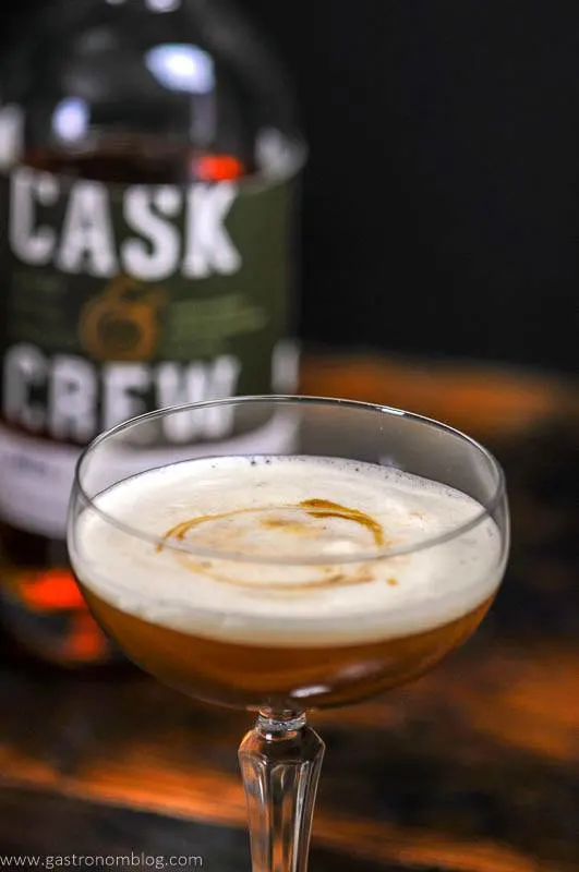 A close up of the Holiday Ginger Flip Cocktail and a bottle of Cask and Crew Ginger Spice Whiskey.