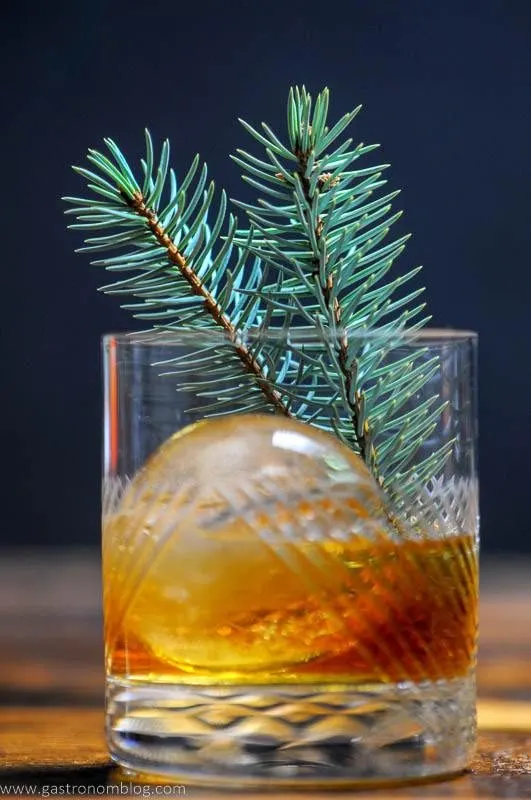 A close up shot of a Pine Old Fashioned Cocktail in a crystal rocks glass on a wooden bar top.