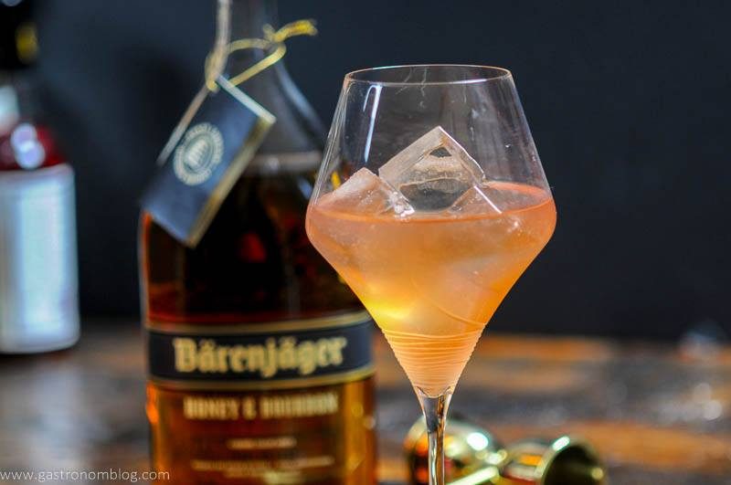 A wine gass sits on a wooden bar top along side a bottle of Barenjager Honey and Bourbon.