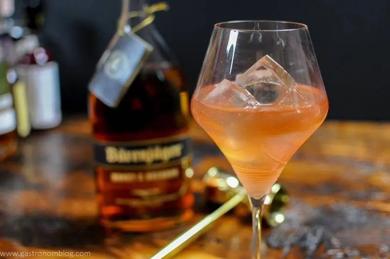 A wine gass sits on a wooden bar top along side a bottle of Barenjager Honey and Bourbon.