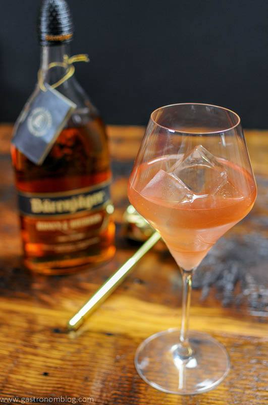 A wine glass sits on a wooden bar top along side a bottle of Barenjager Honey and Bourbon.