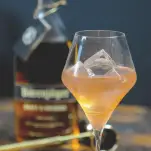 Honey Bourbon Cocktail in a wine glass, whiskey bottle in background