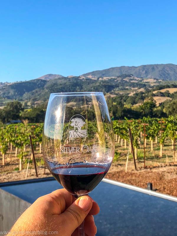 A wine glass filled with red wine from Silver Oak Alexander Valley in front of vines and the hills of Sonoma County.