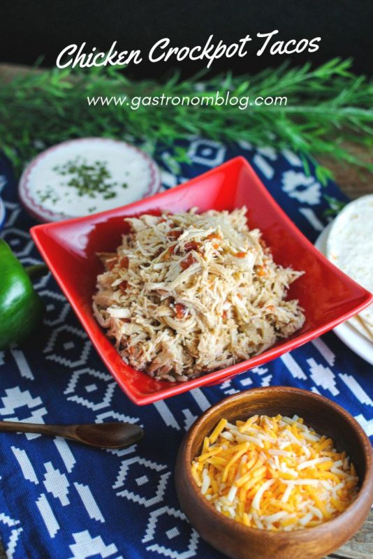 Chicken tacos in red bowl with bowls of cheese, sour cream and tortillas