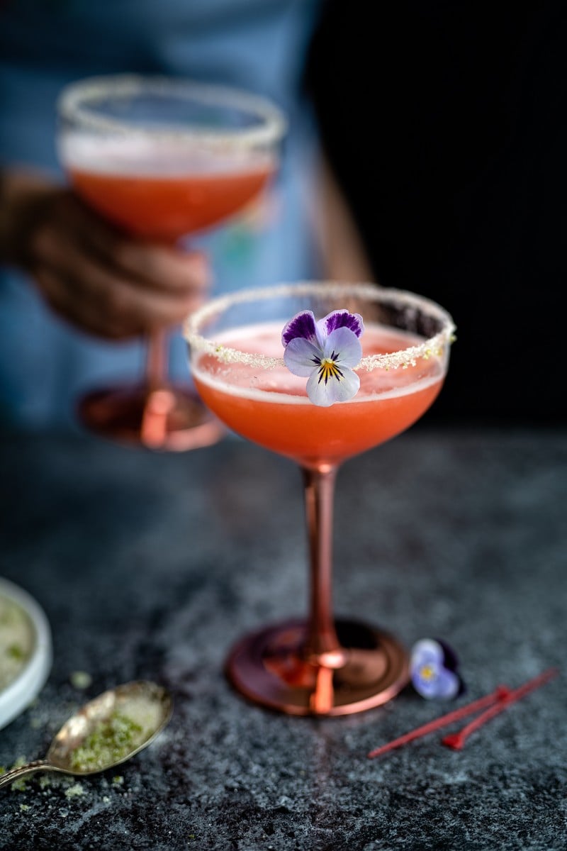 Pink cocktails in coupes with purple edible flowers