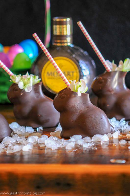 Chocolate Easter Bunnies filled with a cocktail sit on a bar top garnished with spring flowers in front of a bottle of Mozart Dark Chocolate Liqueur.