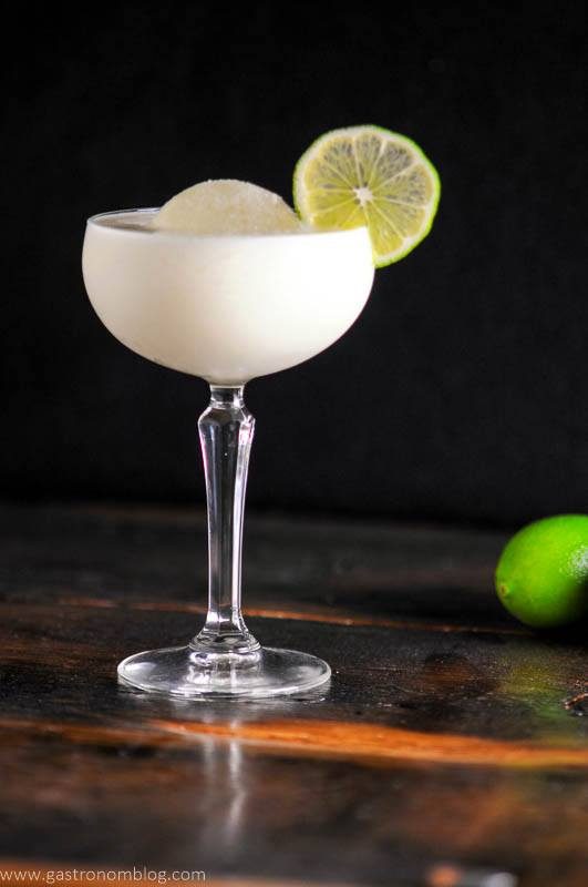 White Chocolate Martini in a coupe glass with ice ball, lime wheel, limes and bottle in background