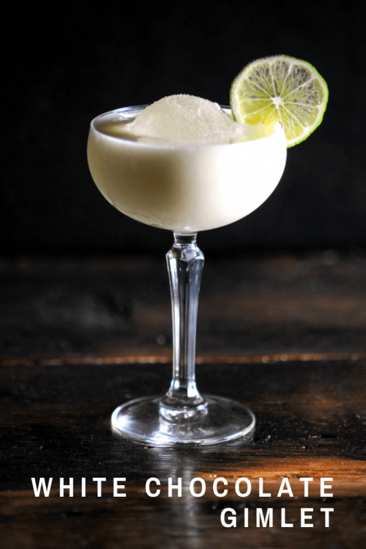 White Chocolate Gimlet in a coupe glass with a large ice ball and a lime wheel. 