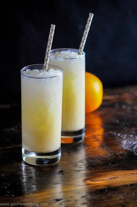 orange dreamsicle cocktail with straws and an orange on wooden board