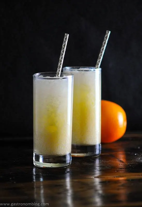 glasses of creamsicle cocktail, purple straws and an orange