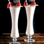 Pink milkshakes in tall glasses. Strawberries and oreos on graham crackers on top, black and white straws