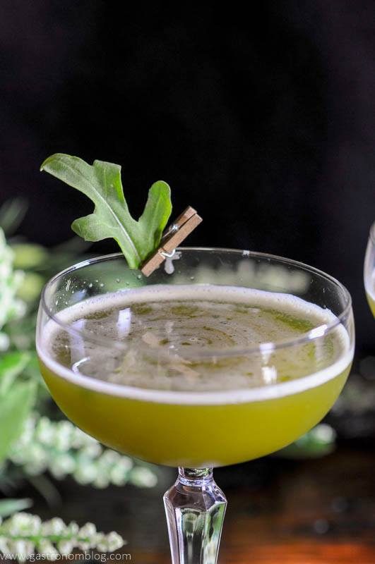 Green cocktail in coupe with leaf pinned to glass