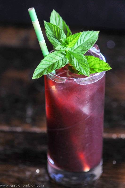Dark red cocktail in high glass, mint, straw