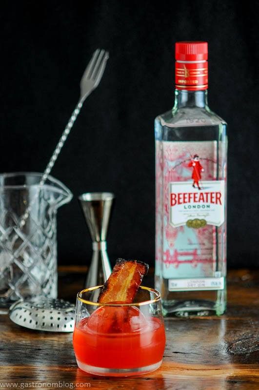 Cocktail in gold rimmed rocks glass with bacon, beefeater bottle behind