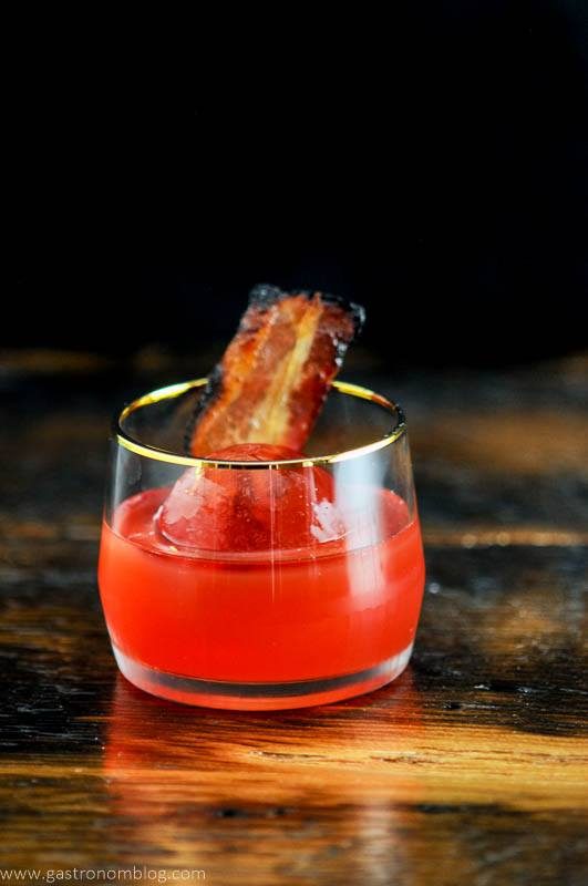 Cocktail in gold rimmed rocks glass with bacon, black background