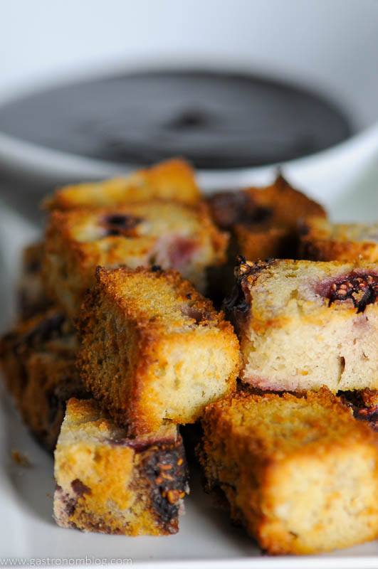 Pound cake cubes on white plate, bowl of chocolate sauce behind