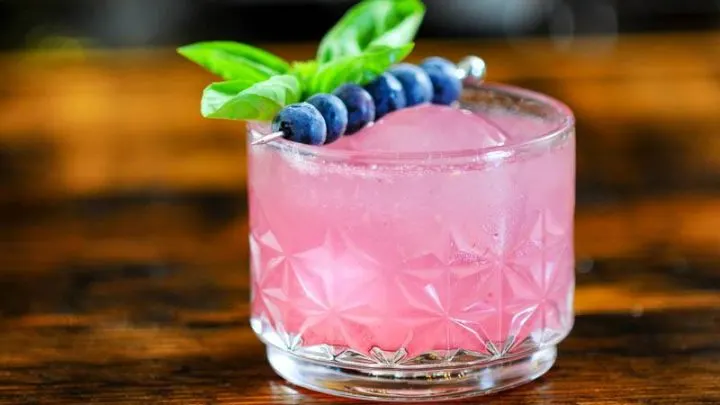 Pink cocktail, blueberries on cocktail pick, sprig of basil