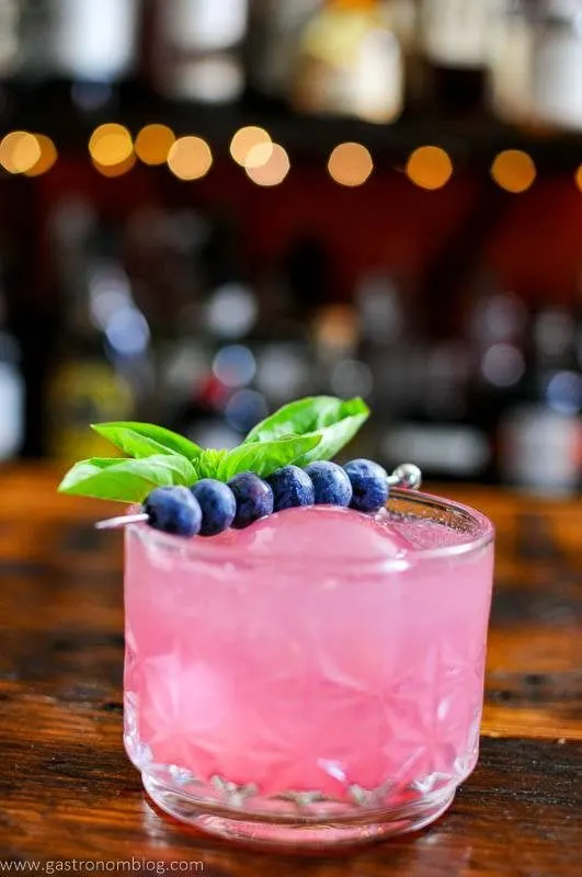 Pink cocktail with berries, lights in background