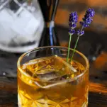 Whiskey cocktail with clear ice in rocks glass, lavender sprigs