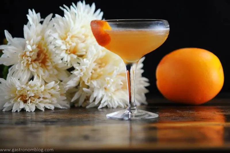 orange cocktail in coupe, white flowers behind
