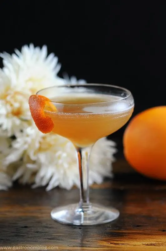 Cocktail in coupe with orange peel, white flowers behind
