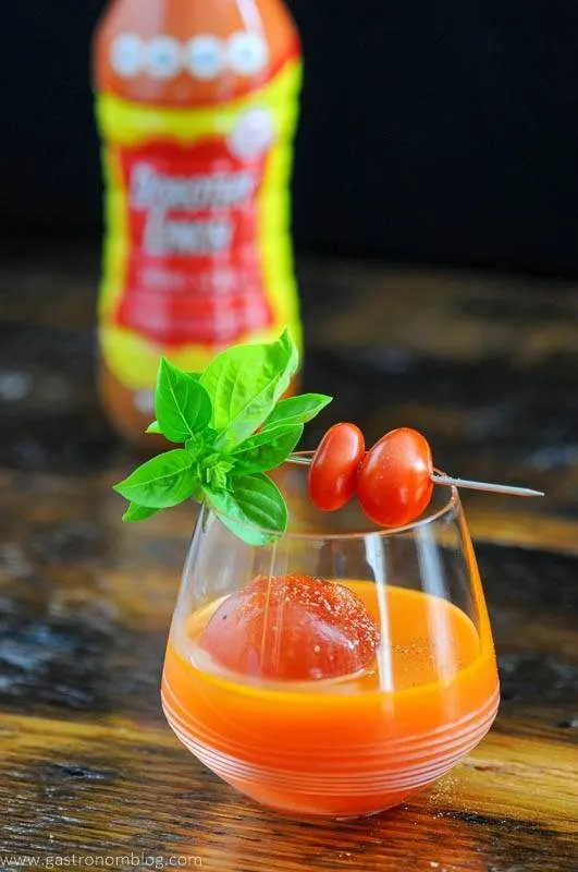 Orange cocktail topped with tomatoes and basil, dressing bottle in background