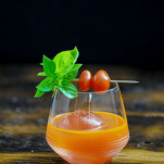Orange cocktail in glass with basil and tomatoes
