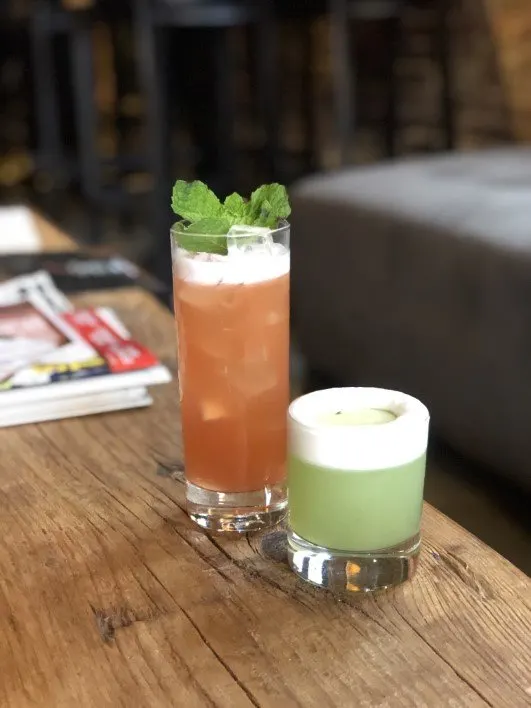 Cocktails at Brazen Open Kitchen in Dubuque, orange colored in tall glass with mint, green in rocks glass with foam