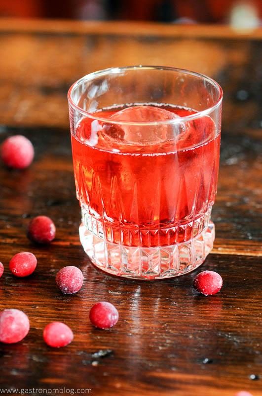 Red Negroni cocktail recipe, cranberries around glass on wood table