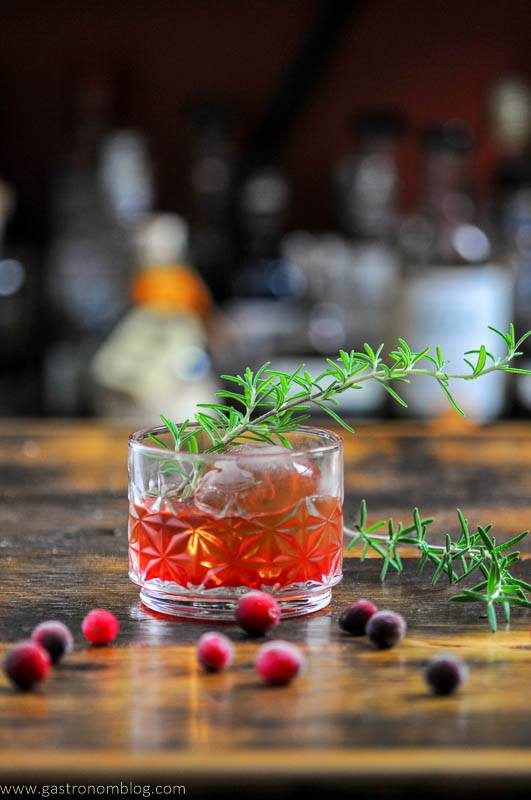 red Cranberry cocktail in rocks glass on wood top, rosemary sprigs