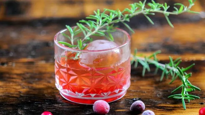 Red cocktail in rocks glass with cranberries and rosemary