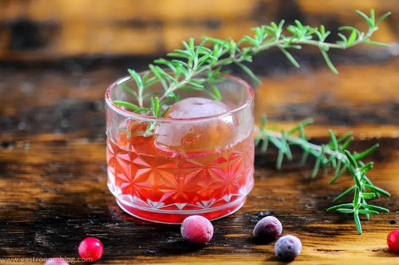 Red cocktail in rocks glass with cranberries and rosemary