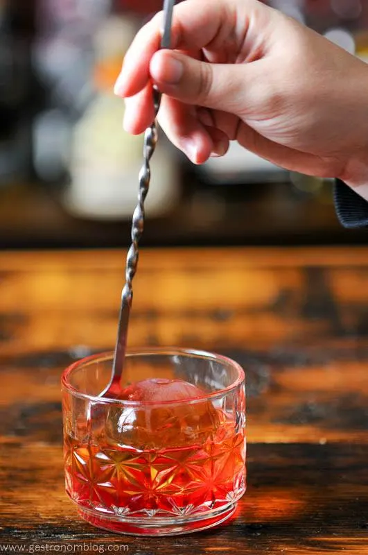Red cocktail being stirred in rocks glass