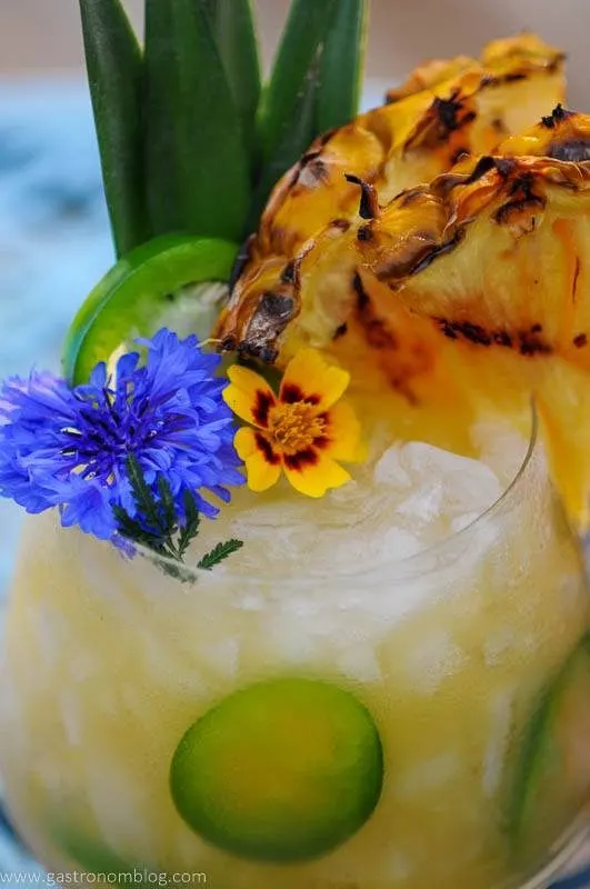 Yellow cocktail with pineapple slice and edible flowers