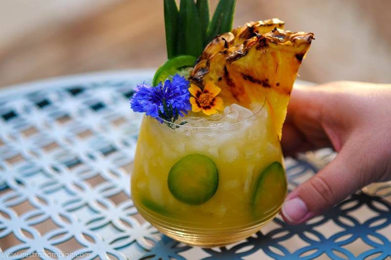 Yellow cocktail with pineapple slice, edible flowers on a blue table