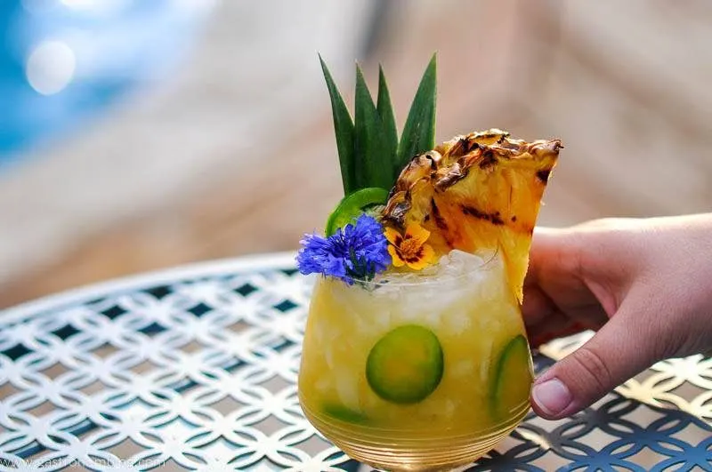 Yellow cocktail on blue table with flowers and pineapple slice