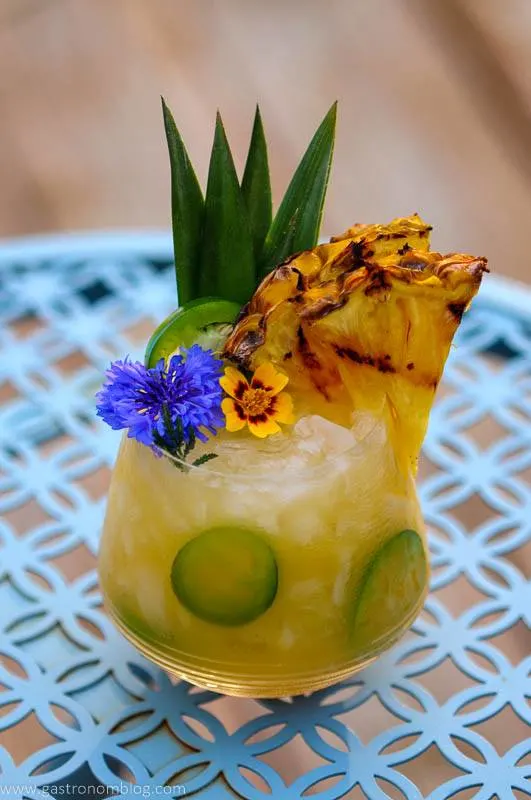 Yellow cocktail with pineapple slice and edible flowers on blue table