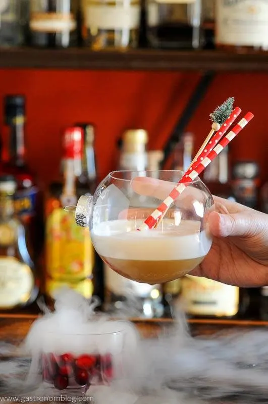 Christmas cocktail being held , dry ice, cranberries and red and white straws