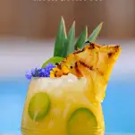 Yellow cocktail in glass with pineapple and flowers