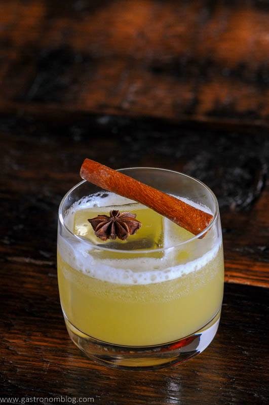 Yellow cocktail in glass with cinnamon stick and star anise on top of ice cube