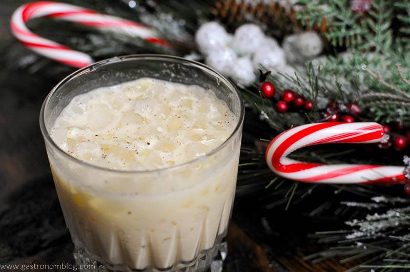 Eggnog cocktail in rocks glass, white cocktail with evergreen and candycanes by glass