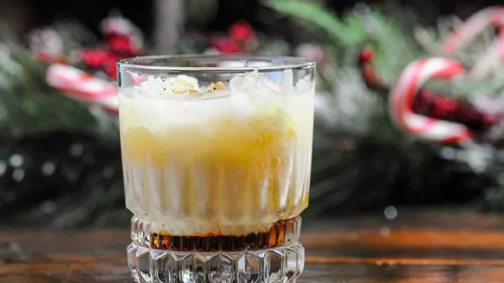 Cocktail in rocks glass, creamy layer on top, brown layer on bottom. evergreen and candy canes in background
